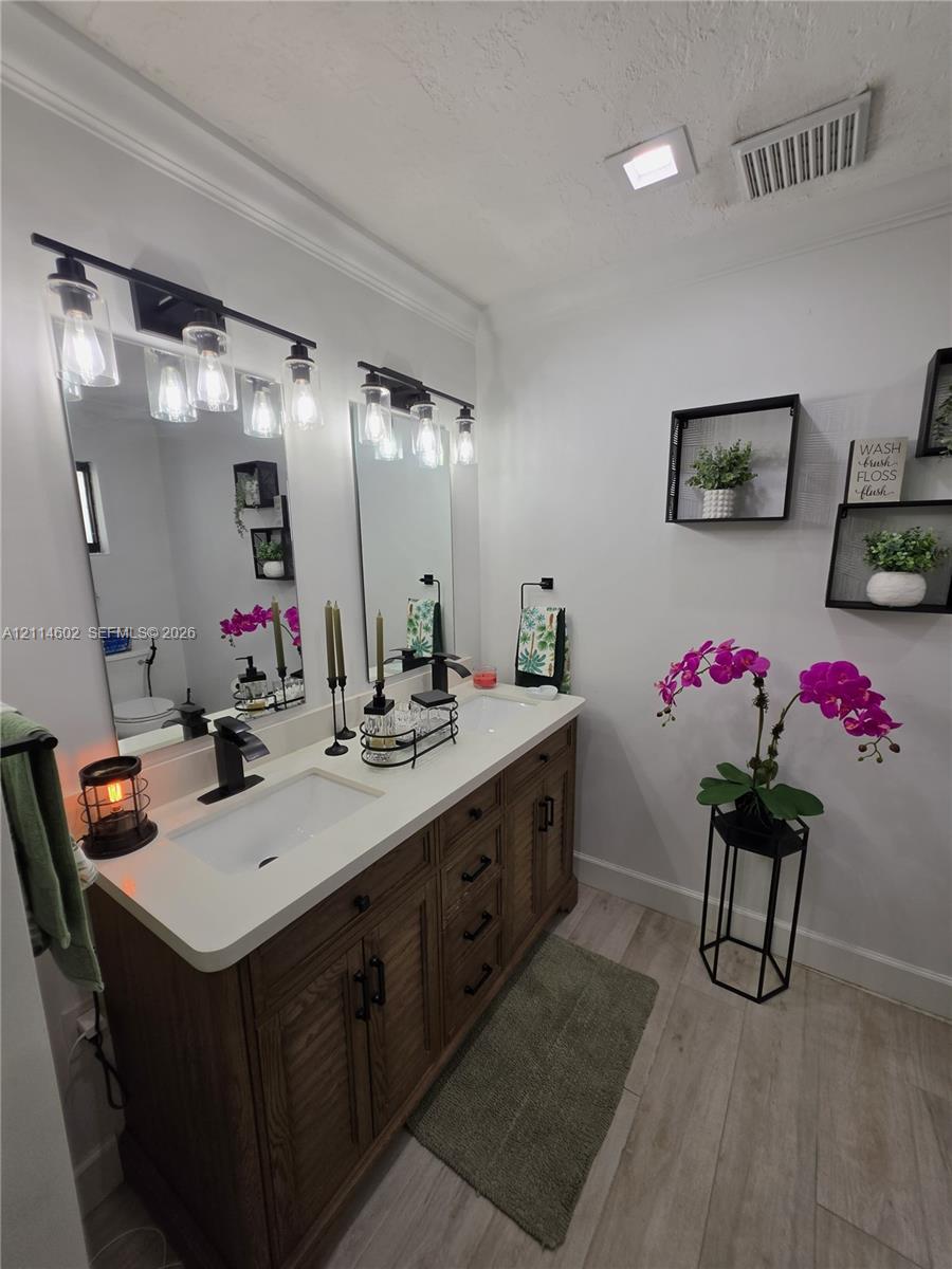Double vanity featuring a light-toned countertop, dual rectangular undermount sinks, wood-finish cabinetry, matte black hardware, and two industrial-style light fixtures