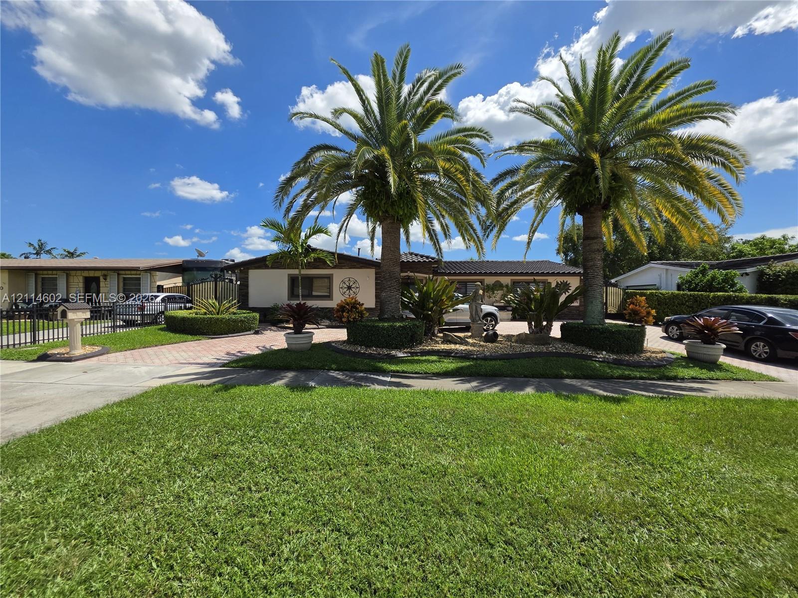 Single-story exterior featuring a paver driveway, mature palm trees, professional landscaping, and a manicured lawn Single-story exterior featuring a paver driveway, mature palm trees, professional landscaping, and a manicured lawn