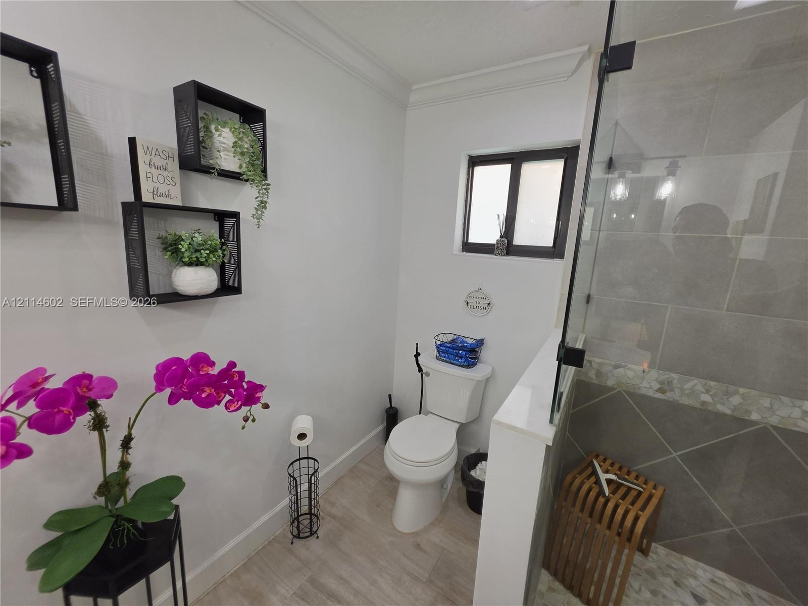 Bathroom featuring wood-finish flooring, a glass-enclosed shower with large-format tile walls, mosaic tile accent border, and built-in wall shelving