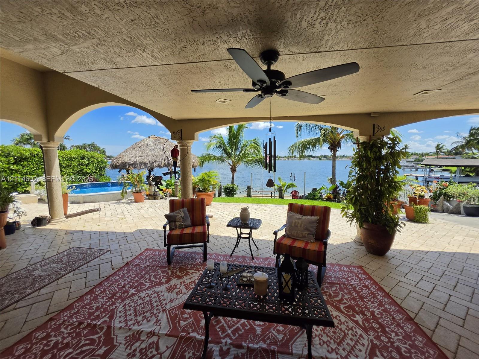 Covered lanai featuring arched columns, paved flooring, and a ceiling fan, overlooking a pool and waterfront