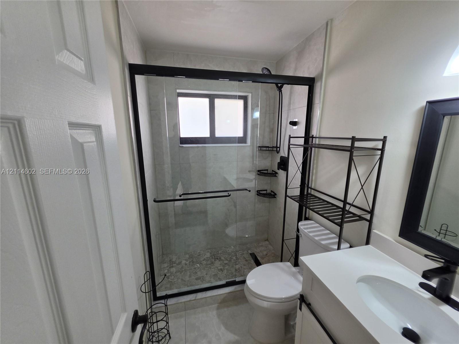 Walk-in shower featuring a sliding glass enclosure with a black frame, tiled wall surround, and pebble-finish shower floor