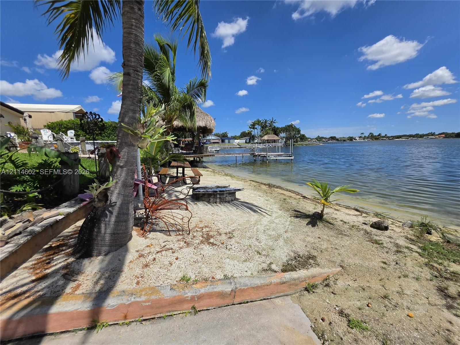 Waterfront property featuring a private sandy shoreline, concrete retaining wall, stone fire pit, thatched-roof gazebo, and private dock