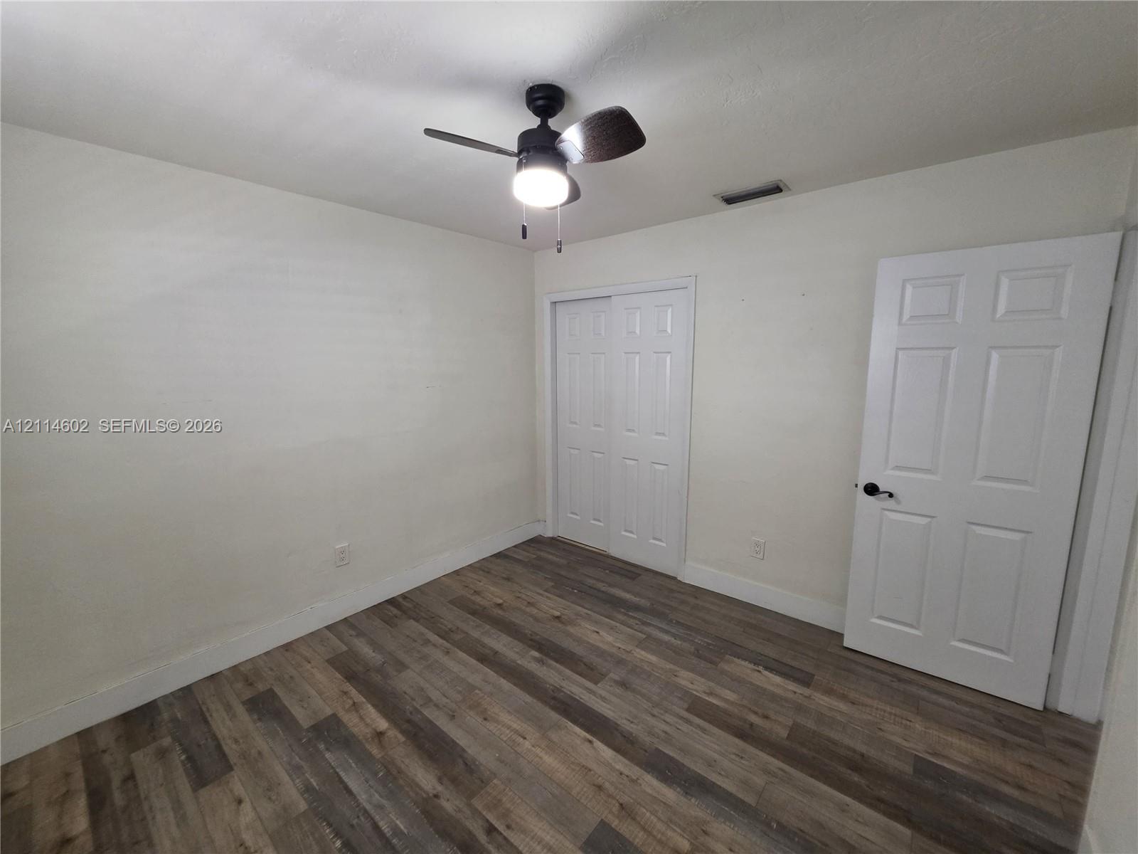 Wood-finish flooring, six-panel interior door with matte black hardware, sliding closet doors, and ceiling fan with integrated lighting
