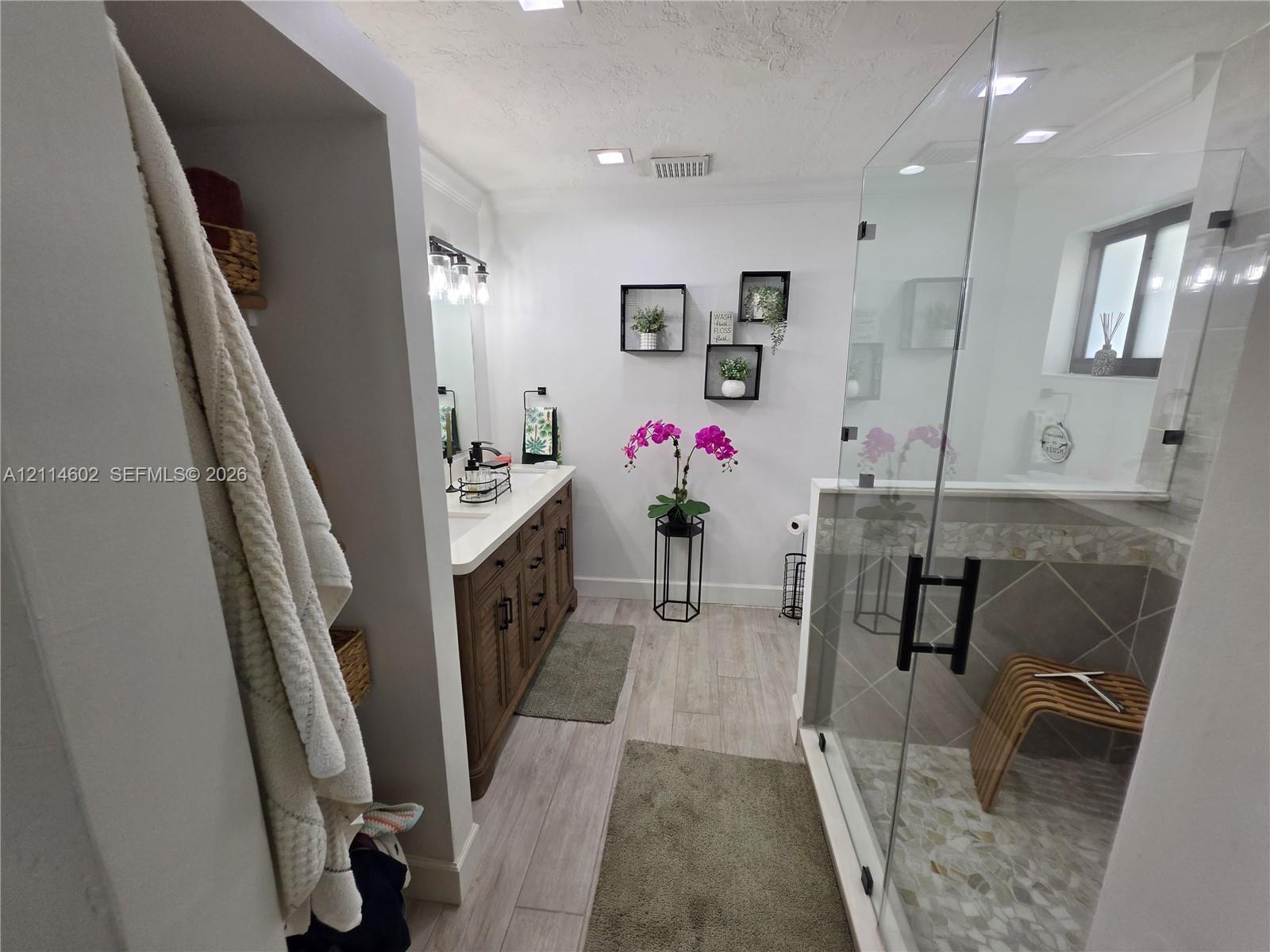 Bathroom featuring a wood-finish vanity with a light-toned countertop, walk-in glass-enclosed shower with tile surround, mosaic floor tiling, and wood-finish flooring