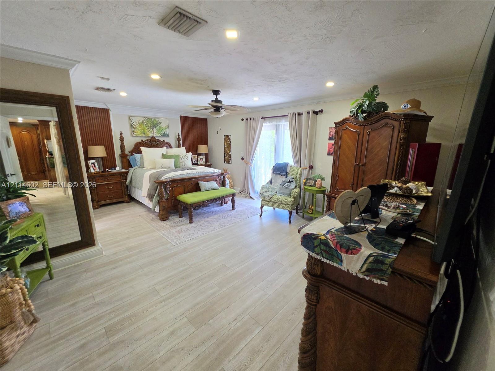 Spacious interior featuring wood-finish flooring, recessed lighting, crown molding, vertical wall paneling, and sliding glass doors