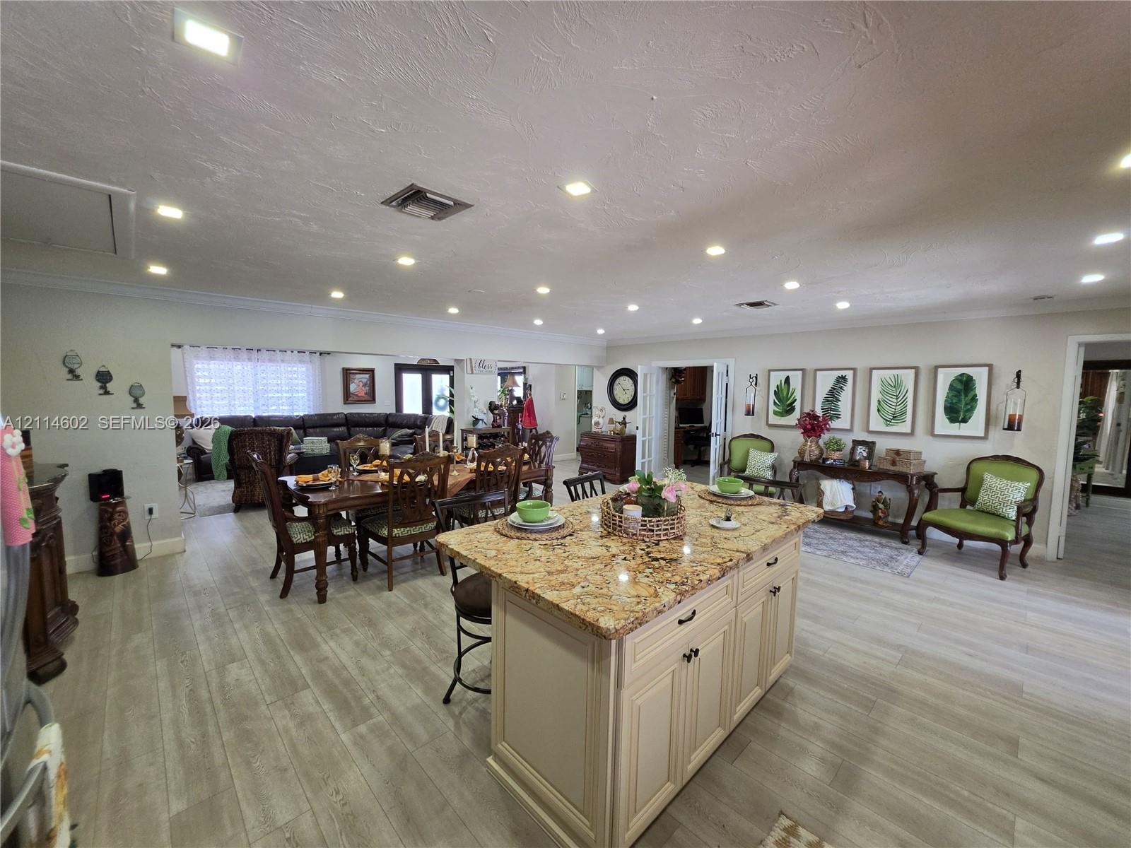 Kitchen featuring an expansive stone-topped island with shaker-style cabinetry, recessed ceiling lighting, and wood-finish flooring throughout