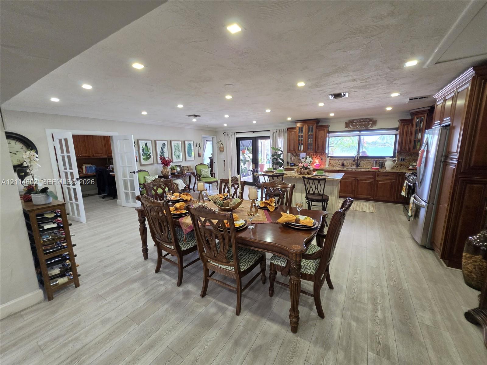 Open-concept kitchen and dining area featuring wood-finish flooring, recessed lighting, stained wood cabinetry, a center island, and French doors