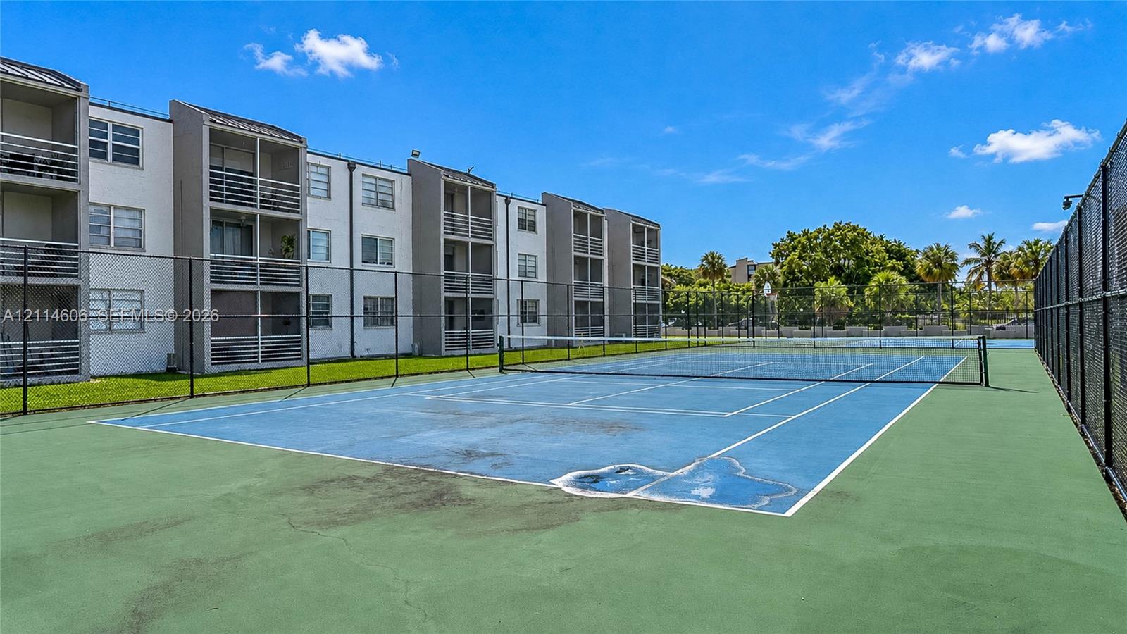 Hard-surface tennis court featuring perimeter chain-link fencing and mesh privacy screening