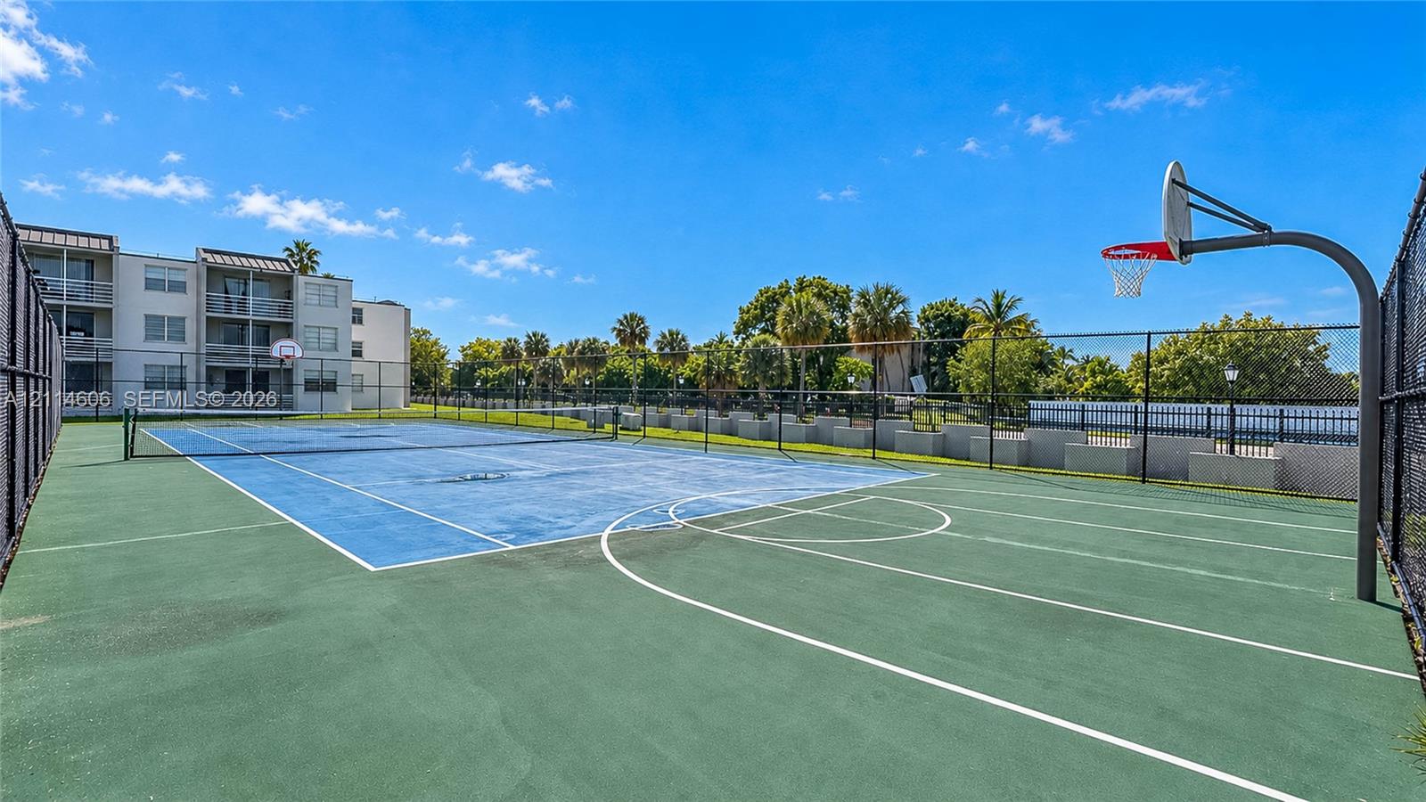 Multi-purpose court featuring a basketball hoop, tennis court markings, chain-link perimeter fencing, and concrete surface