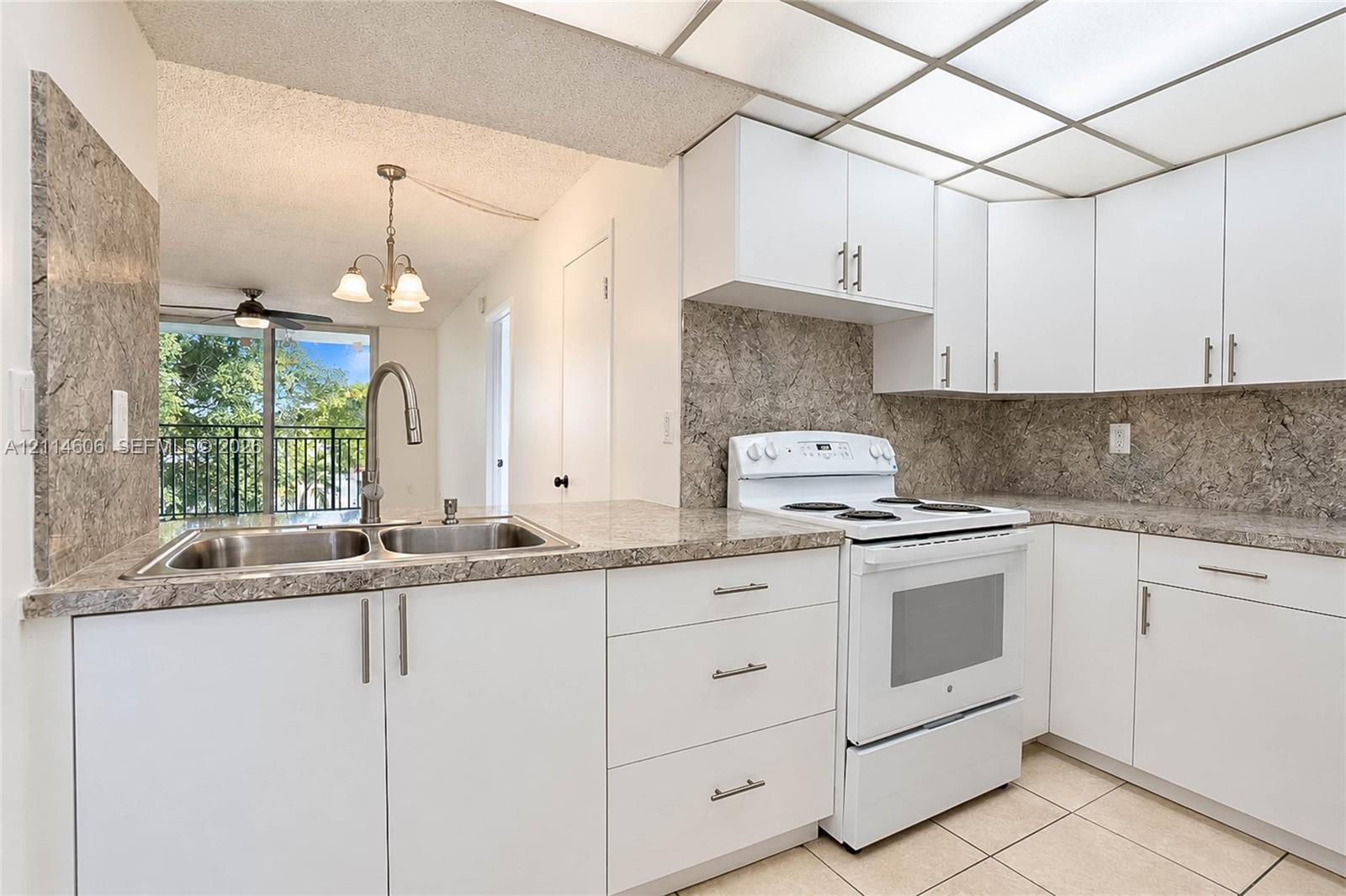 Kitchen featuring white cabinetry with silver-tone hardware, stone-patterned laminate countertops, matching full-height backsplash, white electric range, and double-basin stainless steel sink with high-arc faucet Kitchen featuring white cabinetry with silver-tone hardware, stone-patterned laminate countertops, matching full-height backsplash, white electric range, and double-basin stainless steel sink with high-arc faucet