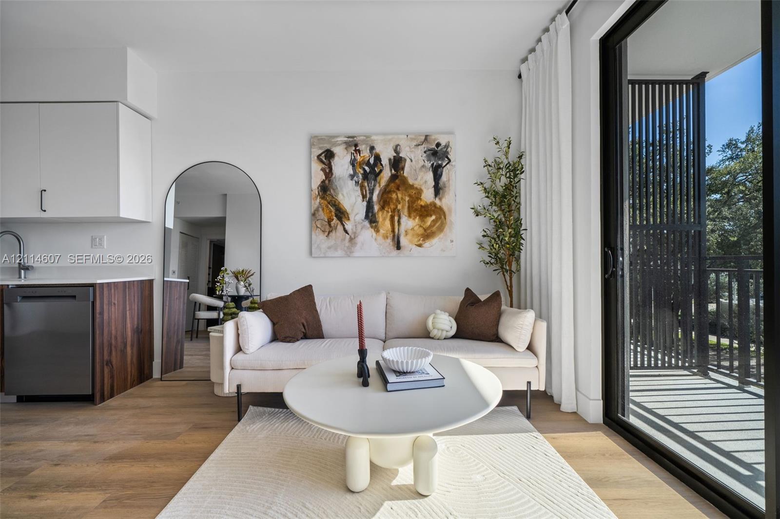 Living area featuring wood-finish flooring, white cabinetry, integrated stainless steel appliances, and large sliding glass doors leading to a railed balcony