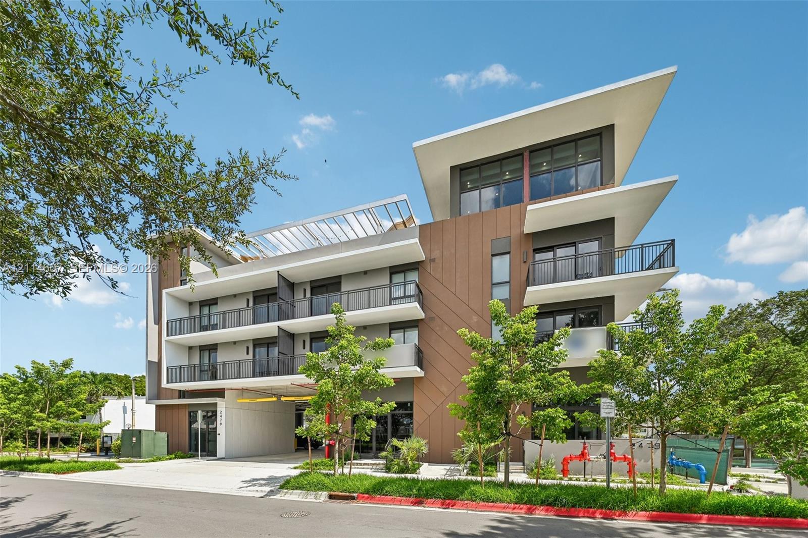 Modern multi-level exterior featuring clean geometric lines, a shed-style roof, wood-tone paneling, metal balcony railings, and covered ground-level parking