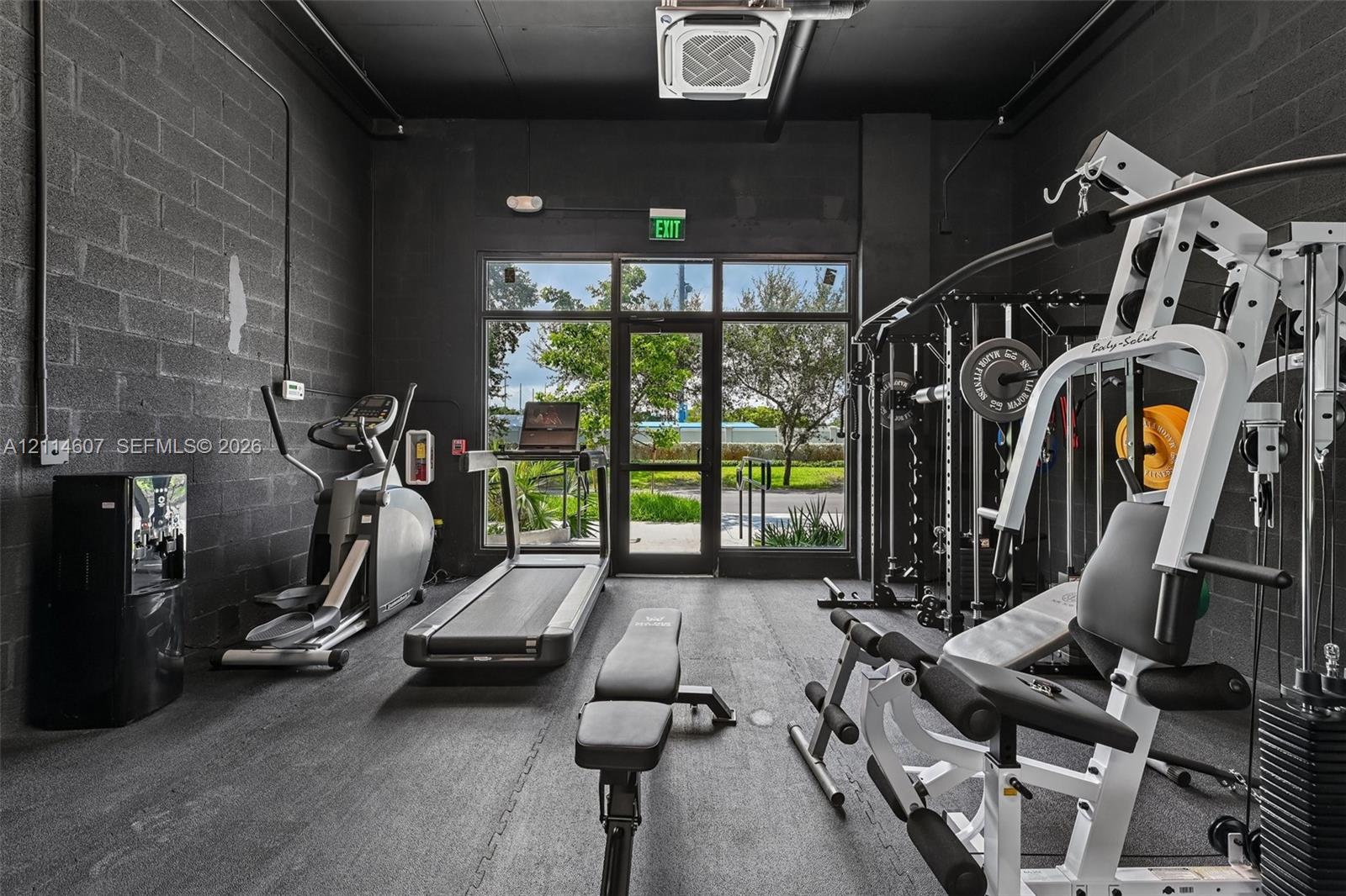 Fitness area featuring painted concrete block walls, durable rubberized flooring, an exposed ceiling structure, and floor-to-ceiling glass paneling with an exterior door