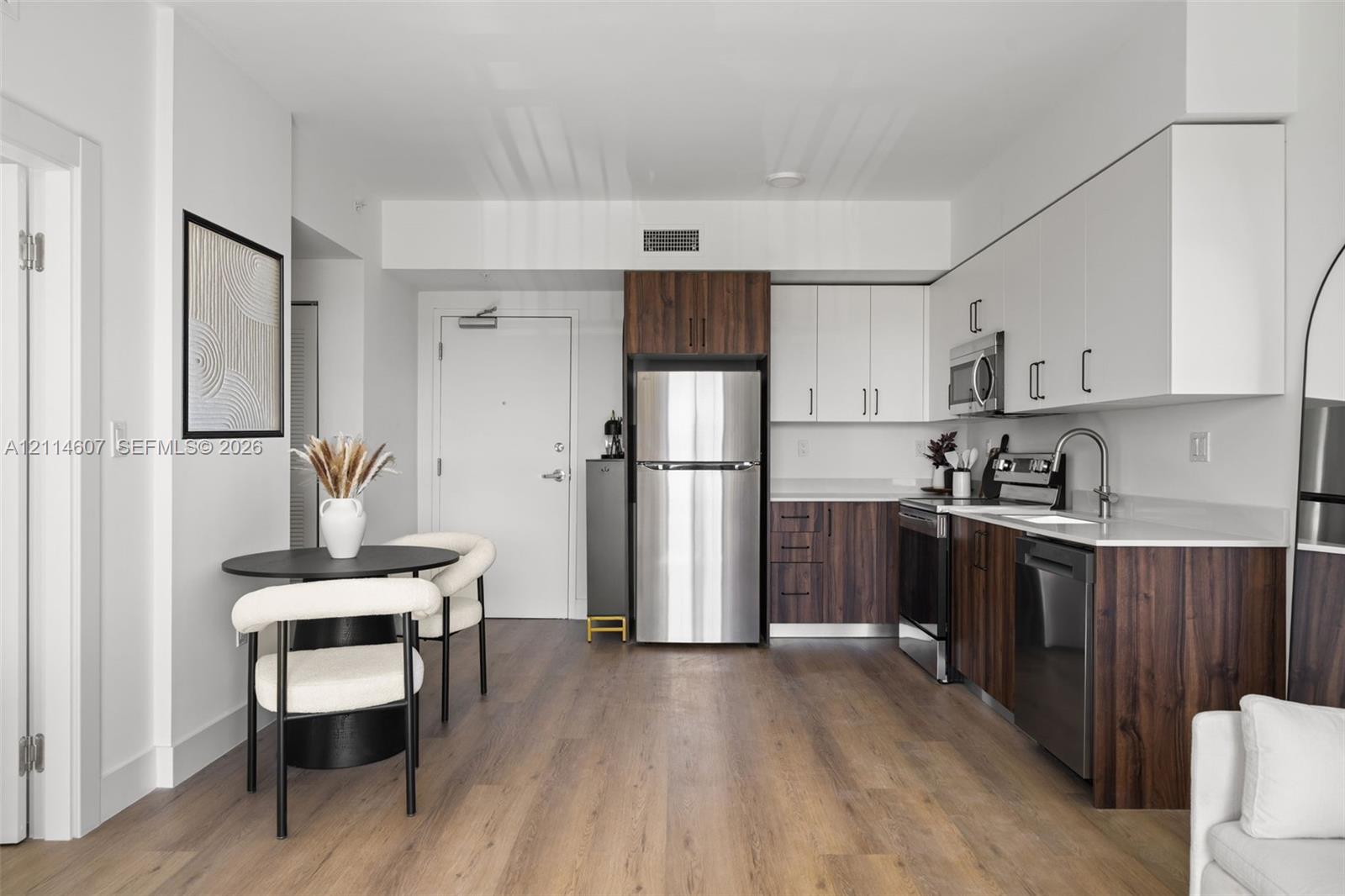 Kitchen featuring flat-panel two-tone cabinetry, quartz countertops, stainless steel appliances, wood-finish flooring, and high-arc faucet