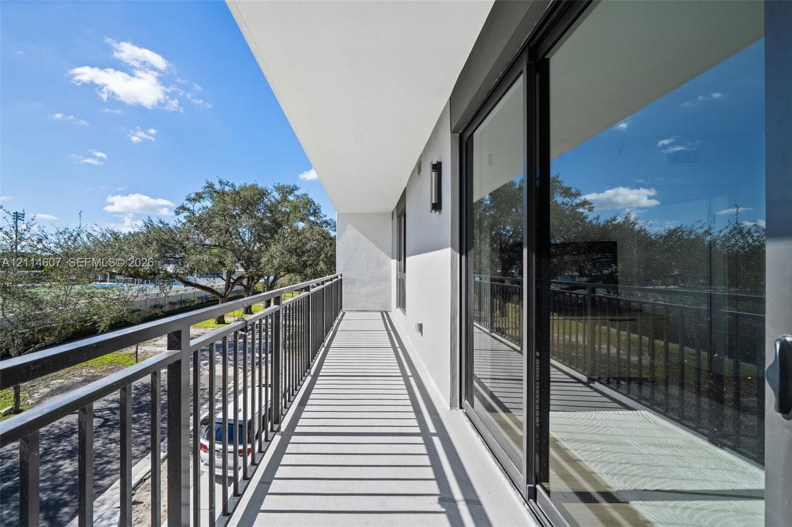 Covered balcony featuring metal railings, concrete flooring, and sliding glass door entry