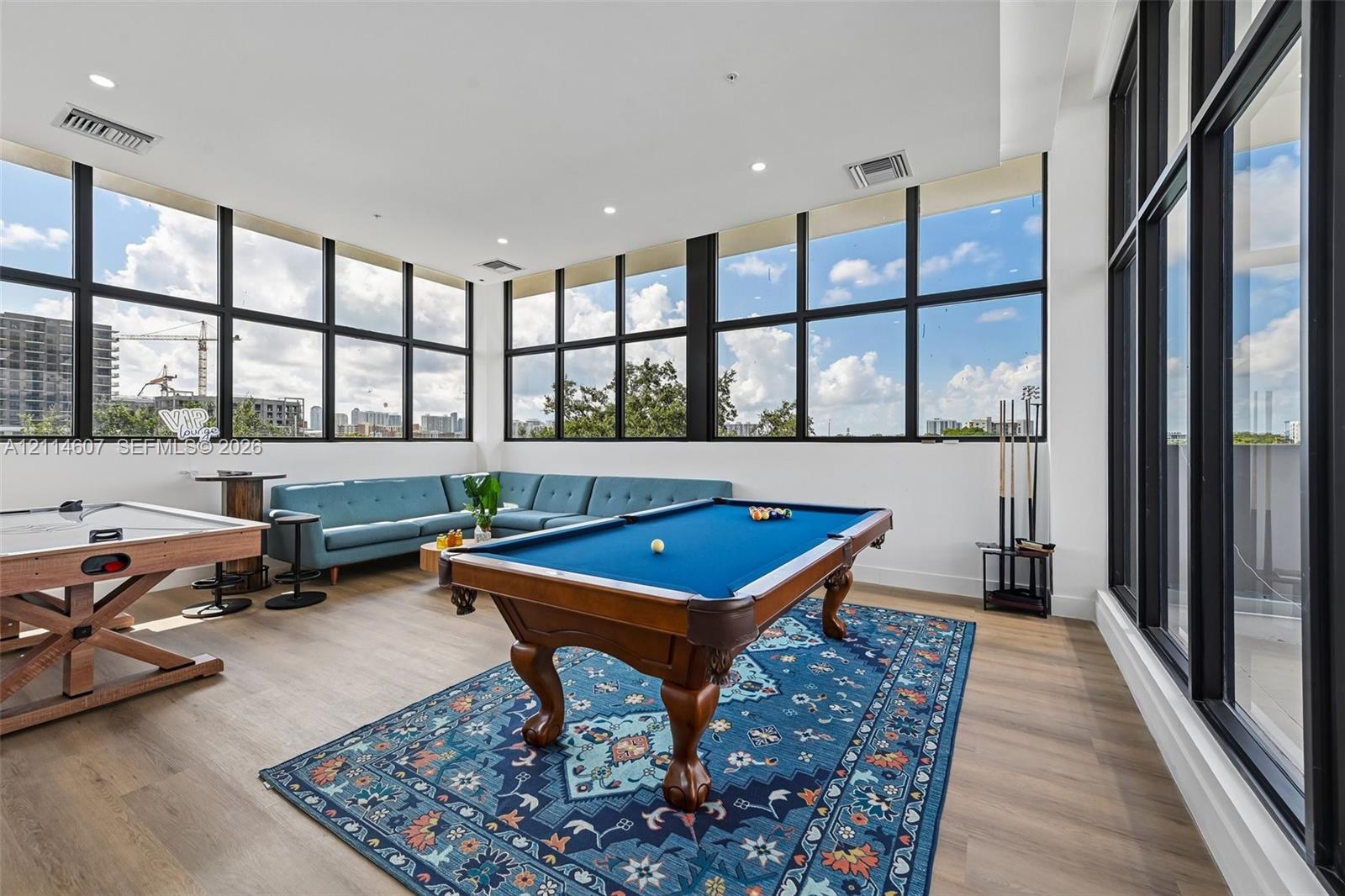 Expansive room featuring floor-to-ceiling windows with black frames, wood-finish flooring, and recessed ceiling lighting