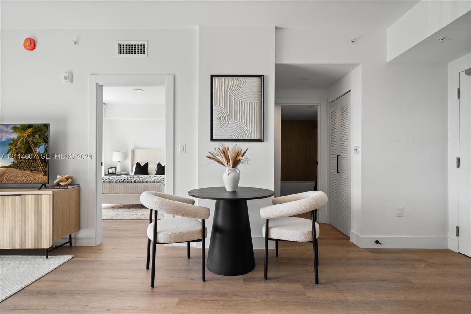 Open-concept interior featuring light wood-finish flooring, crisp white walls, and a dedicated utility closet with louvered doors