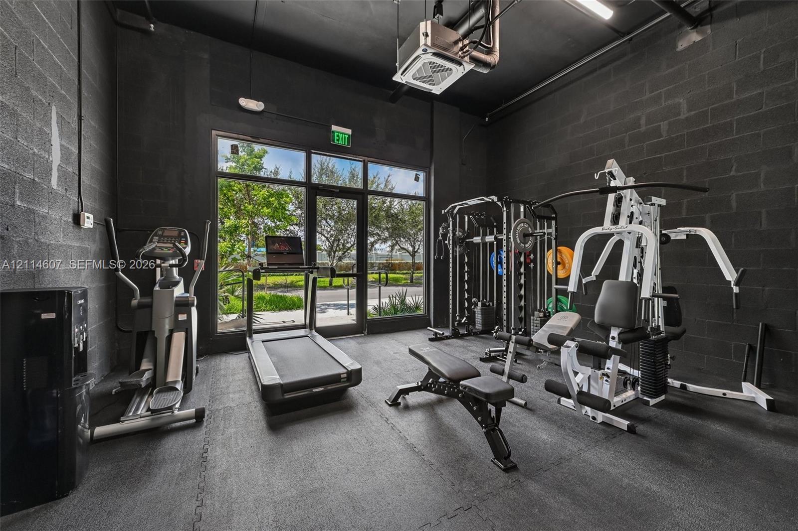 Exposed masonry walls finished in matte black, high ceilings, industrial-style exposed ductwork, rubberized flooring, and floor-to-ceiling glass entry doors