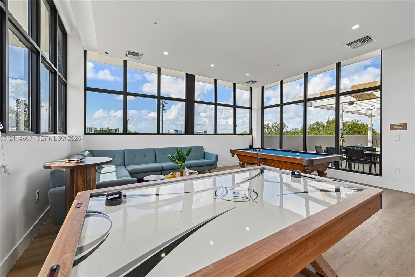 Expansive common area featuring floor-to-ceiling black-frame windows, recessed lighting, and light wood-finish flooring