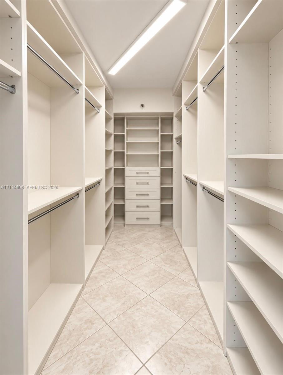 Walk-in closet featuring white built-in shelving, multiple clothing rods, a five-drawer dresser unit, and tile flooring