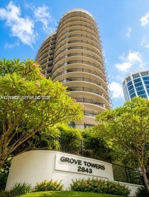 High-rise residential building featuring a curved architectural design, extensive wrap-around balconies, and landscaped grounds
