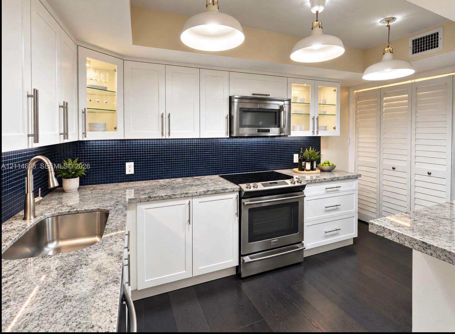 Kitchen featuring white shaker-style cabinetry, stone-surface countertops, blue mosaic tile backsplash, stainless steel appliances