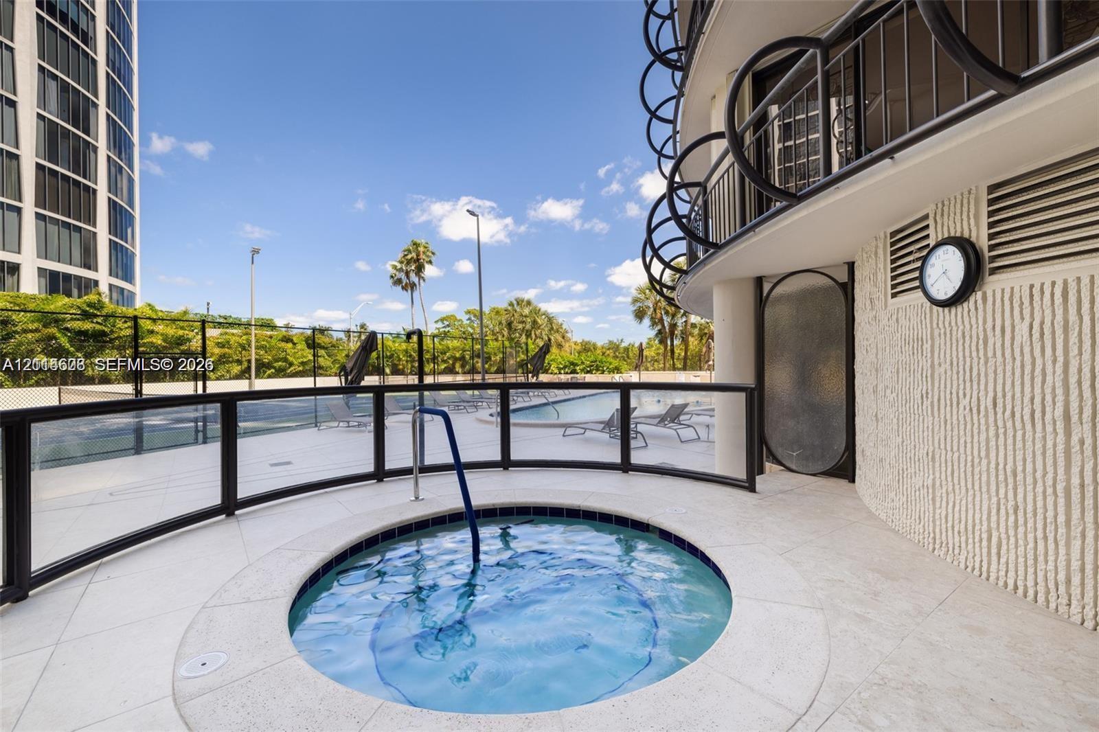 In-ground spa featuring a stone-tile surround, metal handrail, glass-panel perimeter fencing, and textured exterior wall finish