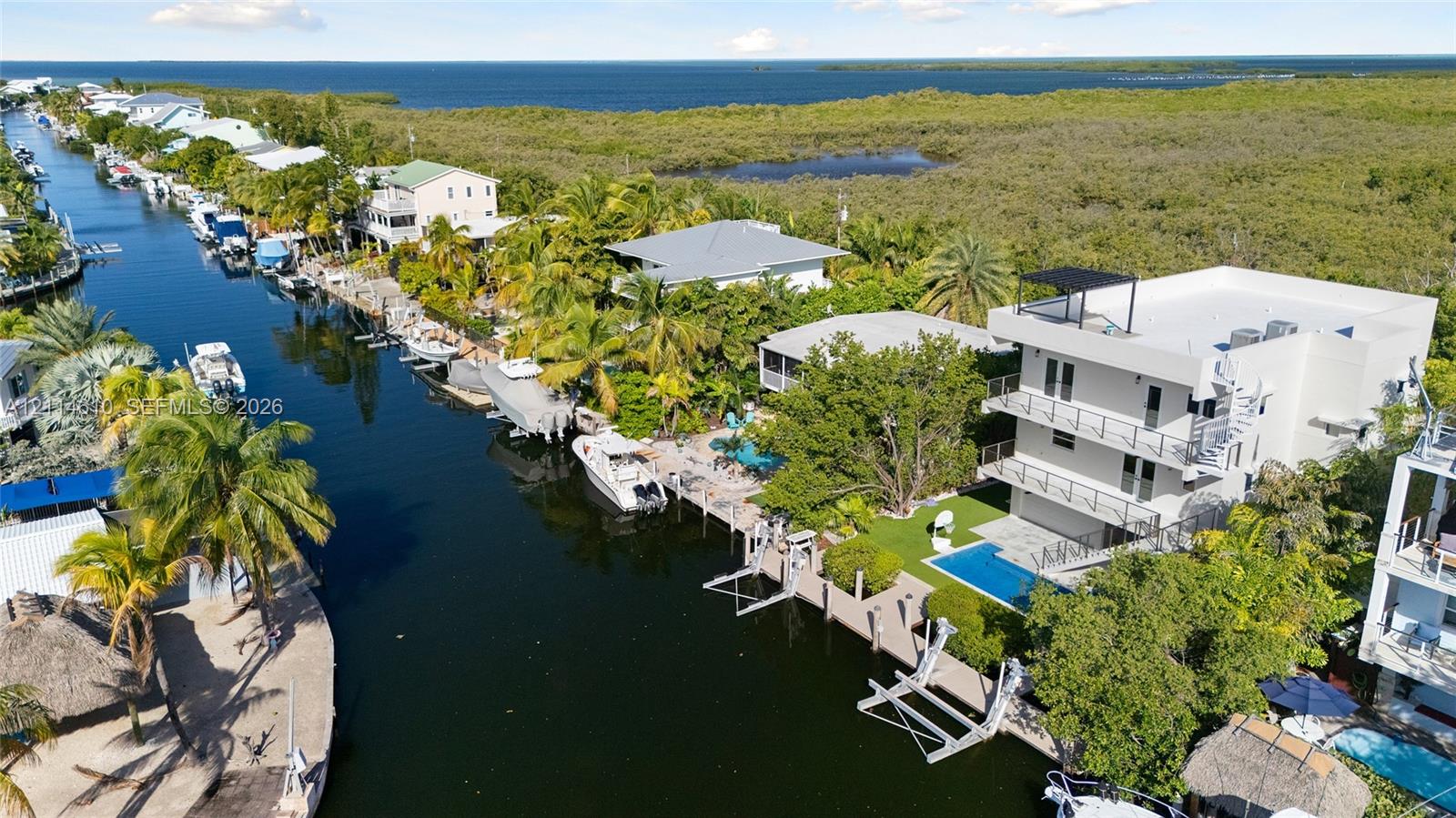 Three-story waterfront residence featuring a private boat dock, rectangular in-ground swimming pool, multi-level balconies with metal railings, and a rooftop terrace