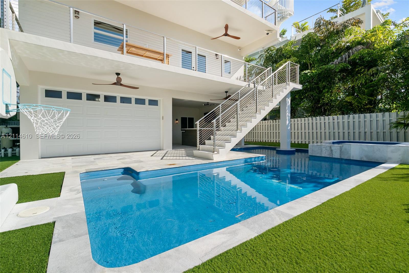 Multi-level exterior featuring a swimming pool, integrated spa, synthetic turf, stainless steel cable railing, and covered patio space