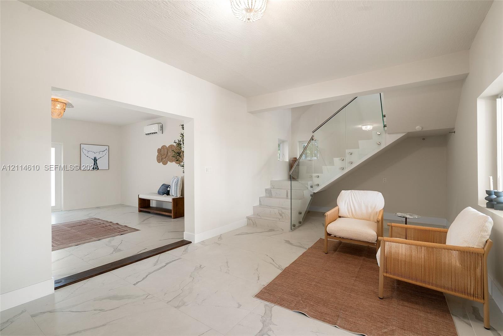 Large-format stone-finish flooring featuring prominent veining, open-riser staircase with glass balustrade, wall-mounted air conditioning unit, and flush-mount decorative ceiling lighting