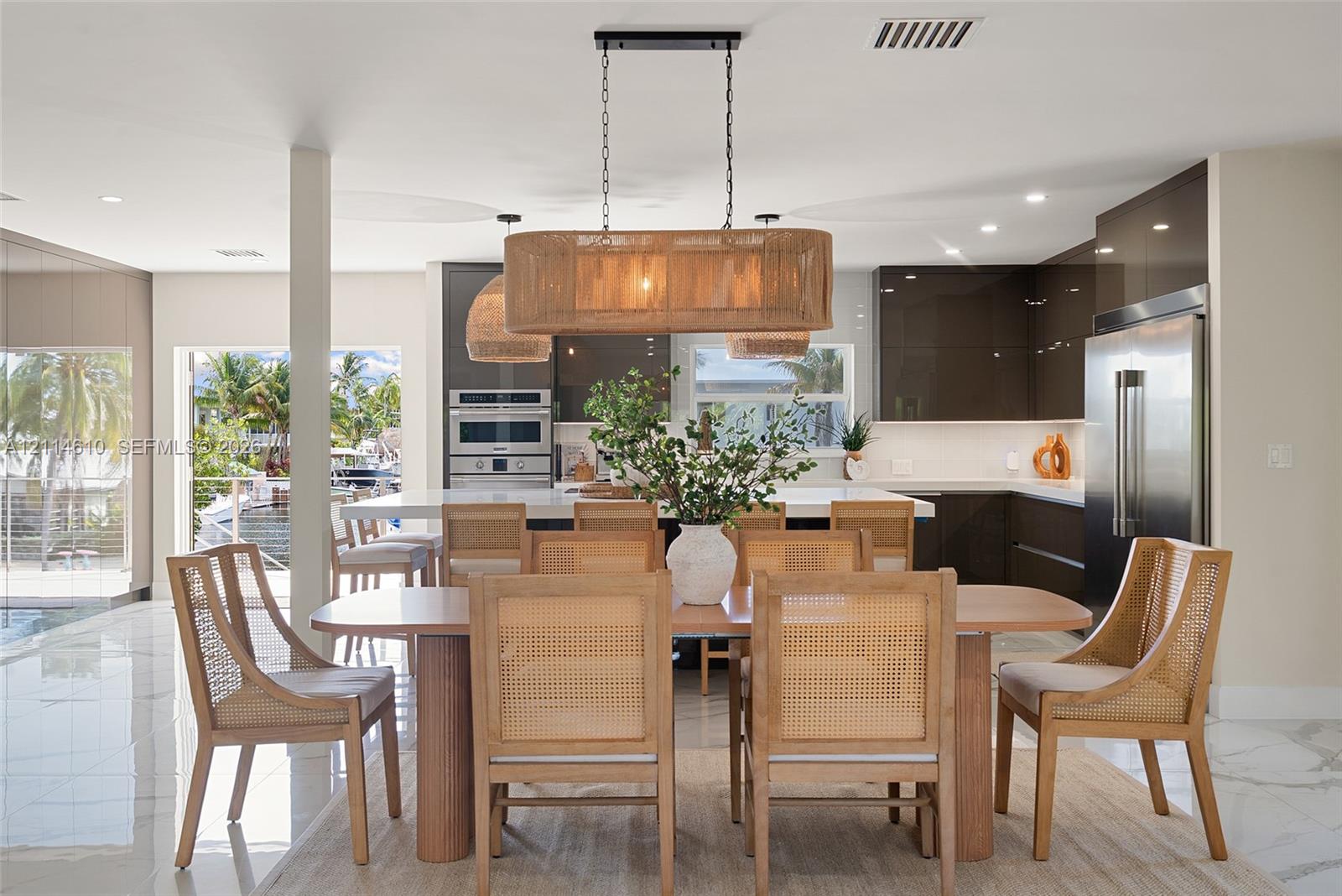 High-gloss cabinetry, stone-surfaced kitchen island, large-format tile flooring, stainless steel built-in appliances, and pendant lighting