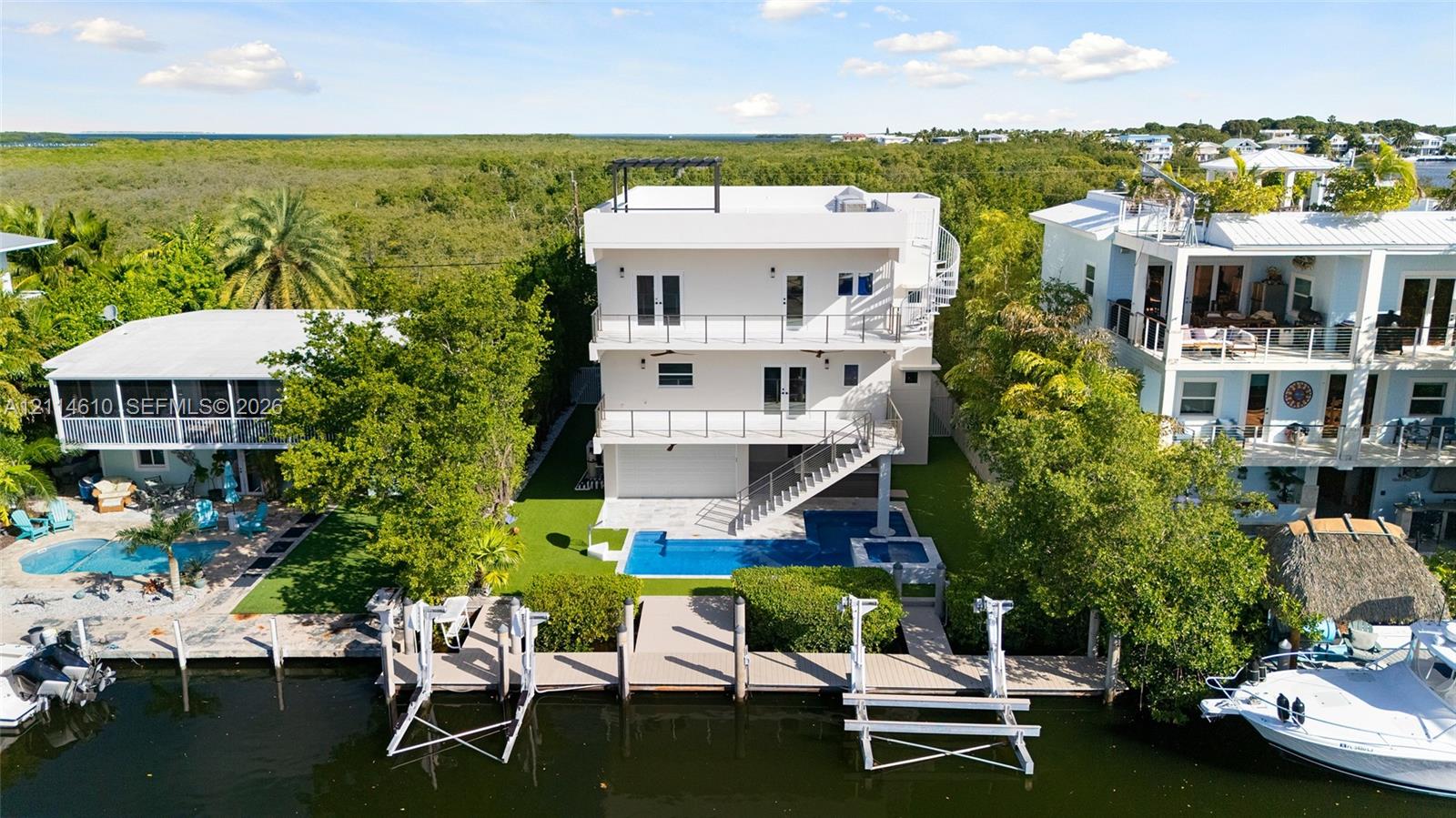 Multi-level coastal residence featuring three stacked balconies, a private swimming pool with integrated spa, and a bulkhead-reinforced canal dock with dual boat lifts