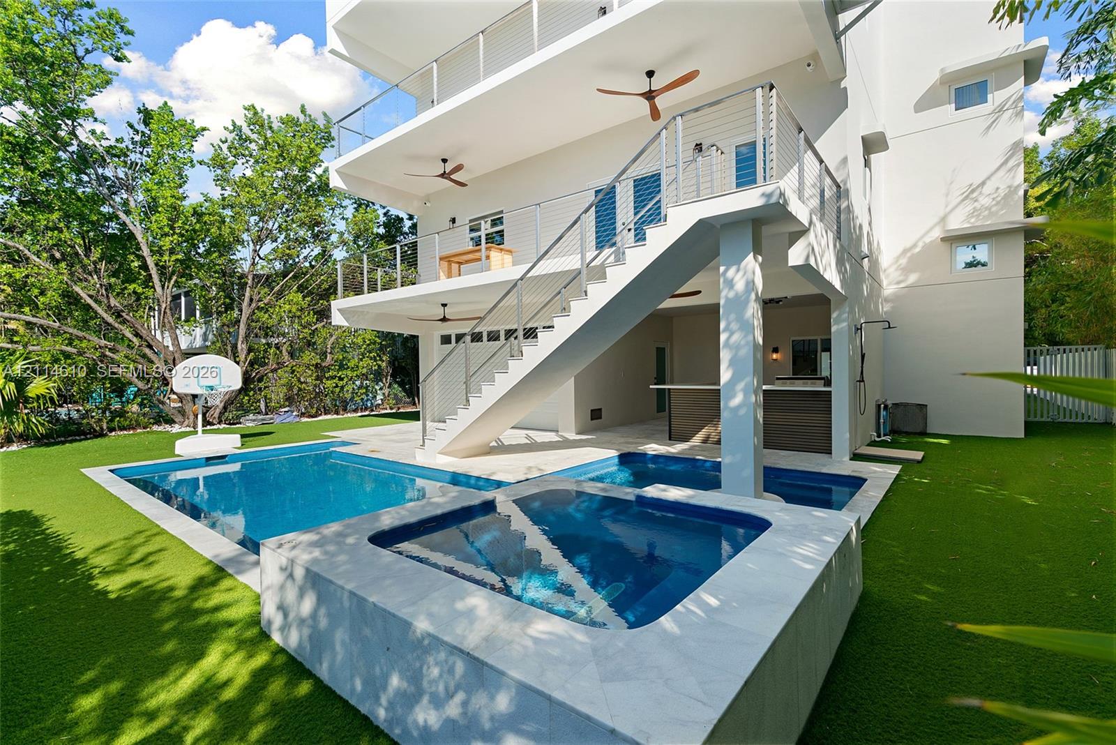 Multi-level exterior featuring a private swimming pool with integrated spa, covered outdoor kitchen with bar seating, and metal cable railing staircase