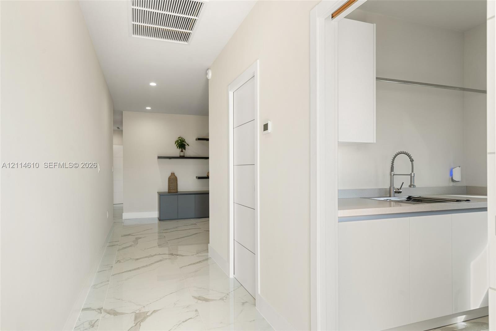 Hallway featuring polished stone-finish flooring with veining detail, recessed ceiling lighting, a five-panel interior door, and built-in cabinetry with wall-mounted shelving