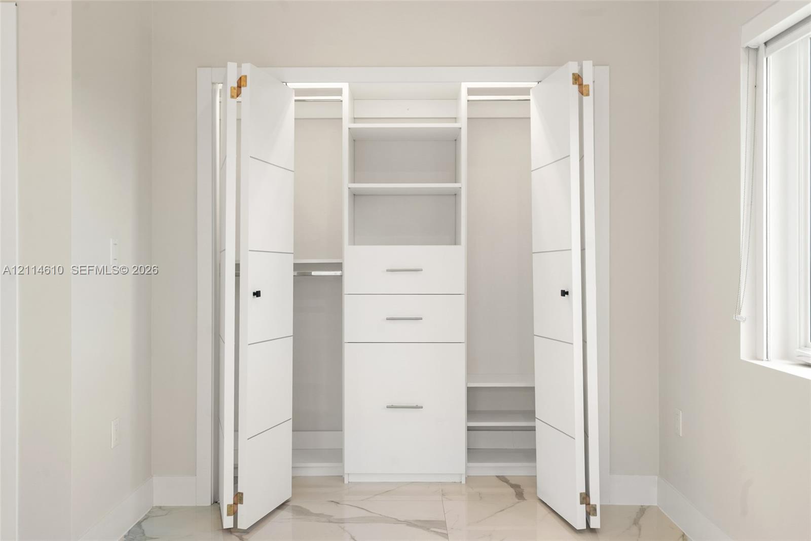 Built-in storage closet featuring white bi-fold doors, center cabinetry with three drawers and shelving, and dual hanging rods