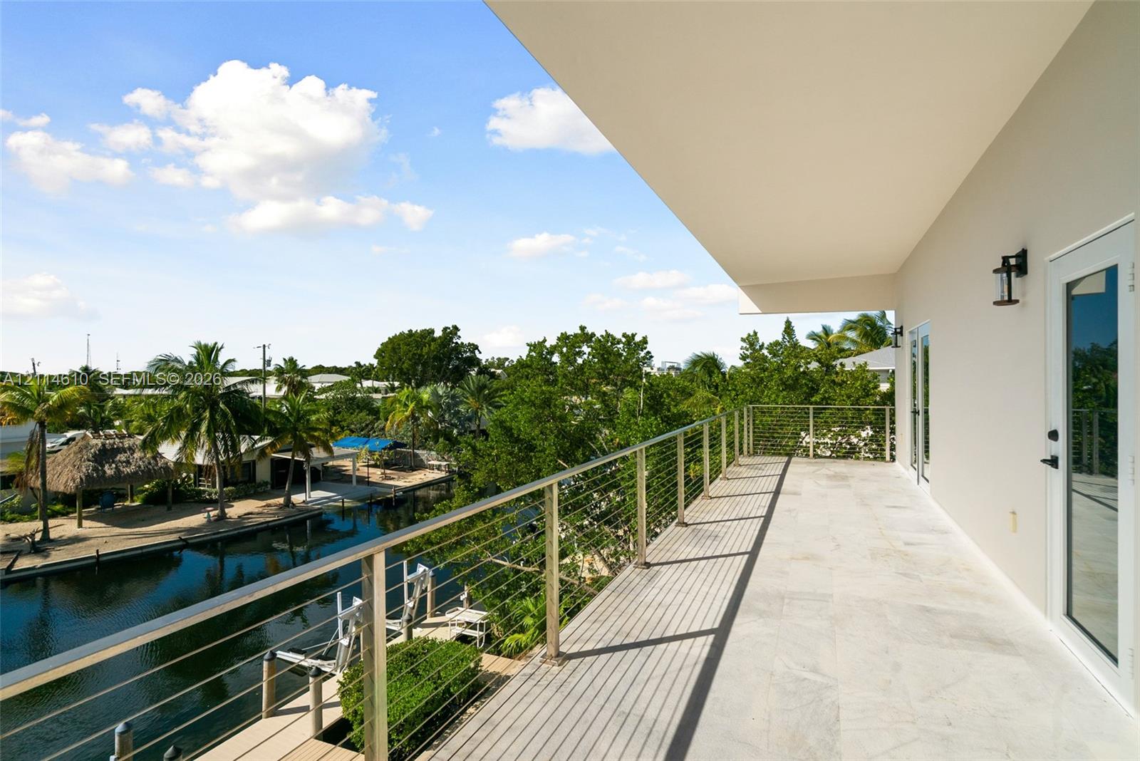 Covered balcony featuring stone flooring, a stainless steel cable railing system, and wall-mounted exterior lighting