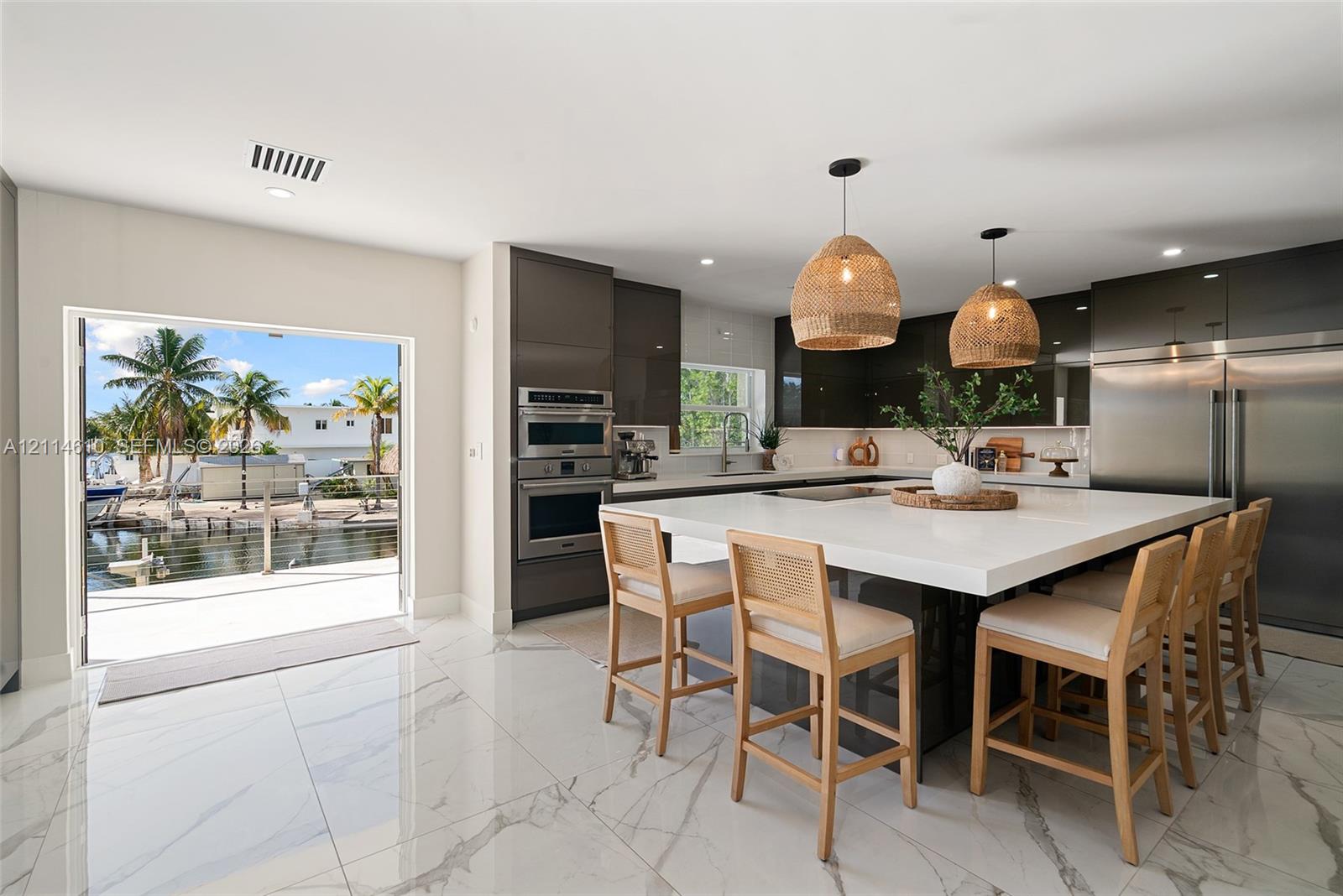 Contemporary kitchen featuring high-gloss cabinetry, a central island with a solid-surface countertop, built-in stainless steel appliances, large-format tile flooring, and woven pendant lighting