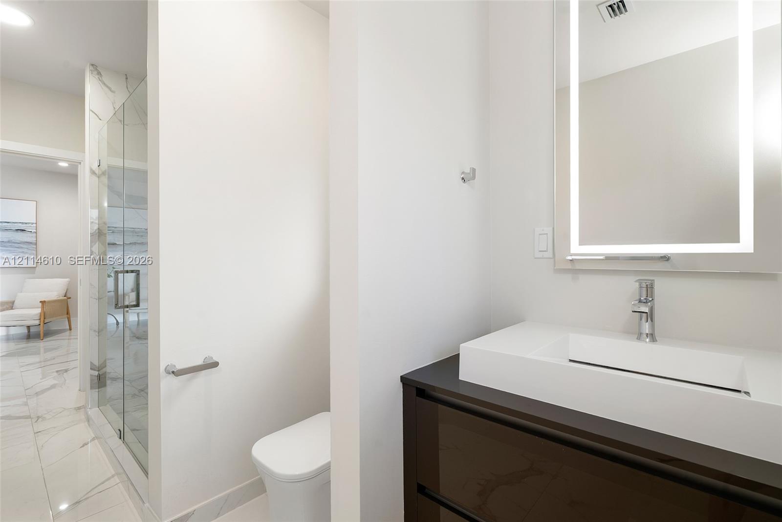 Floating vanity with integrated sink, stone-surface countertop, LED-backlit mirror, glass-enclosed shower with large-format tile surrounds, and tile flooring
