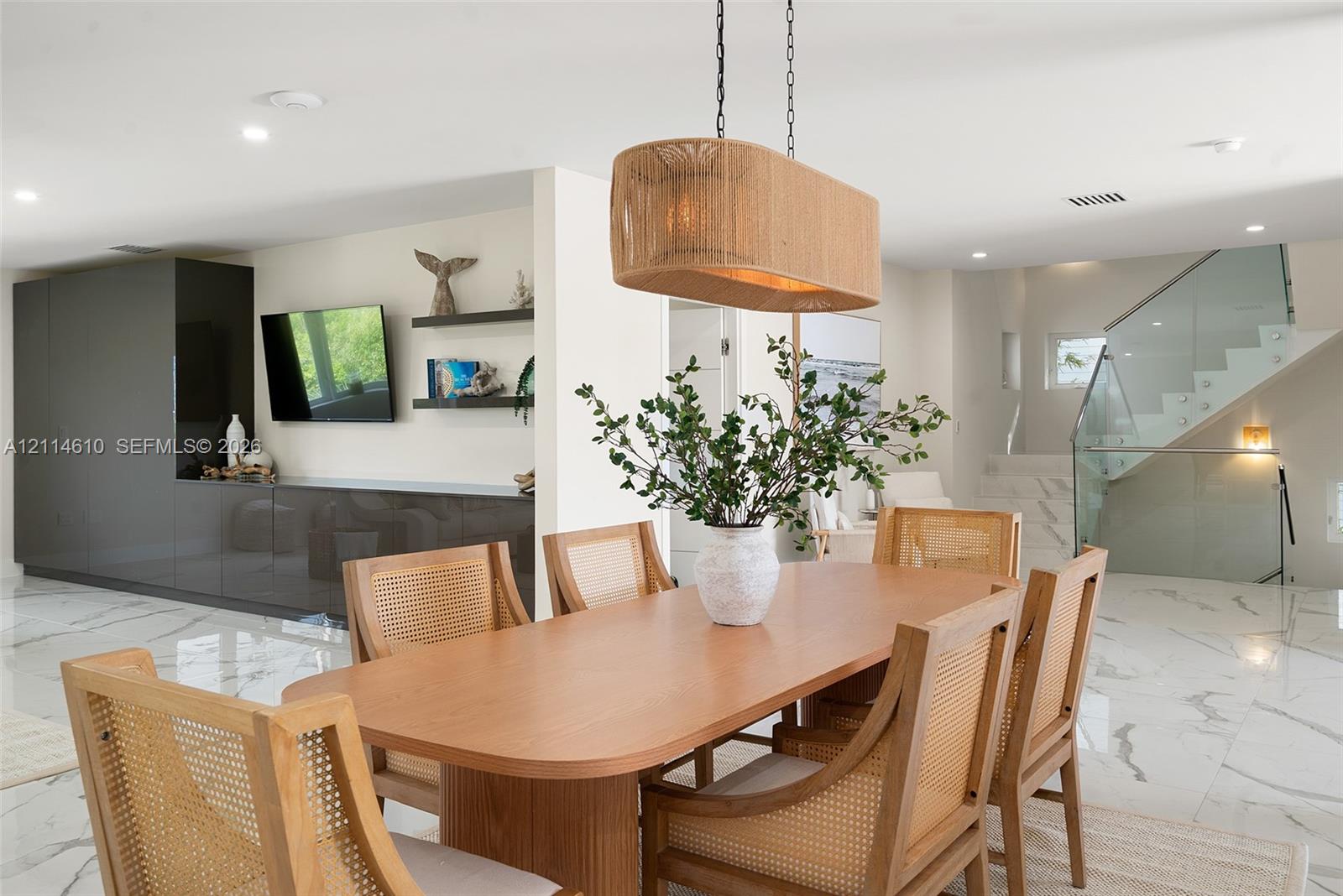 Large-format tile flooring, built-in charcoal cabinetry with integrated shelving, glass staircase railing, and a textured pendant light fixture