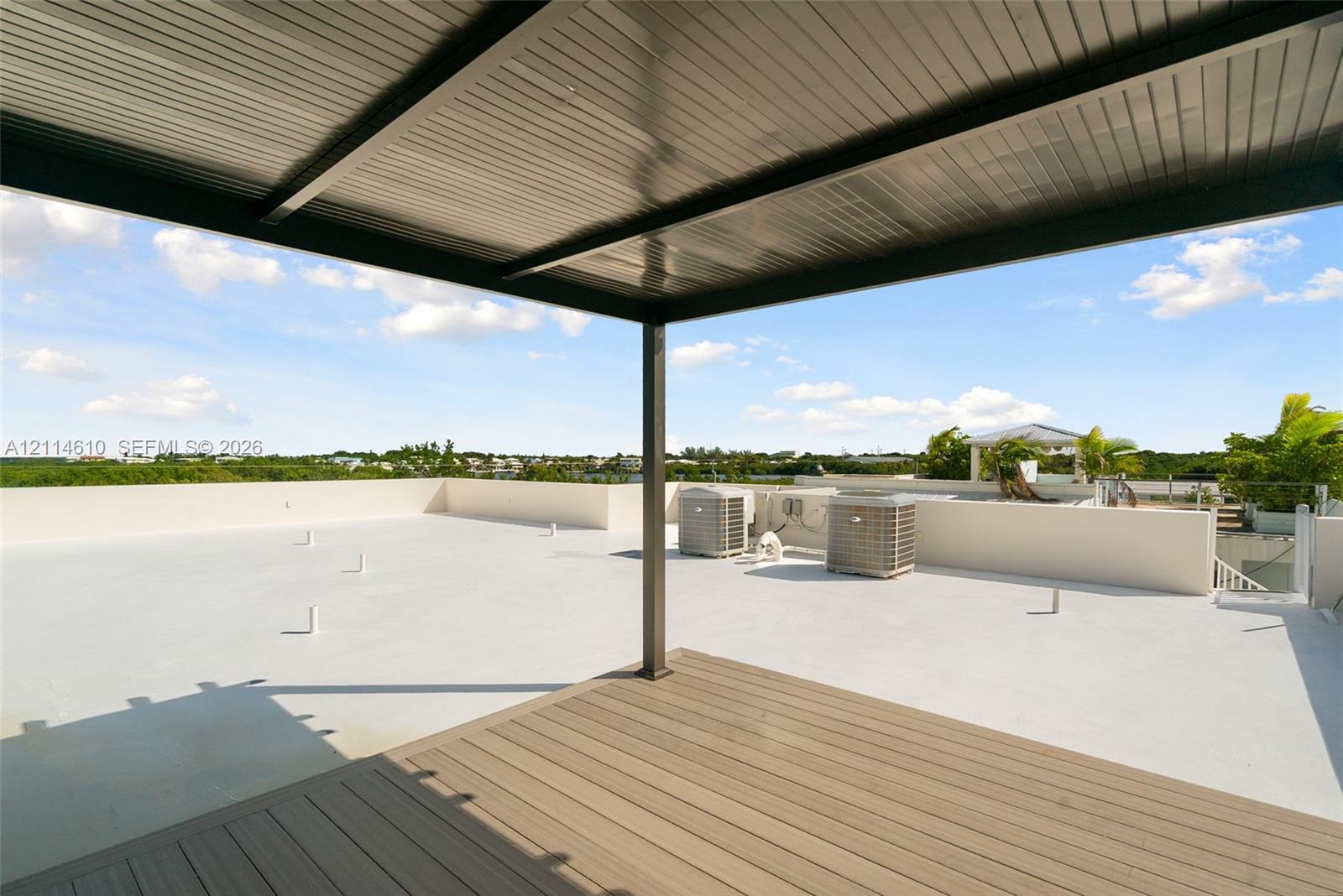 Expansive rooftop terrace featuring a composite wood-finish deck, covered metal pergola, solid perimeter walls, and glass balustrade railing