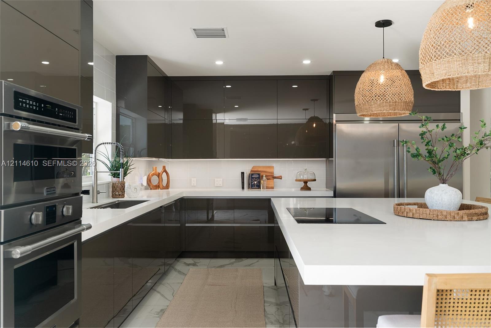 Kitchen featuring high-gloss cabinetry, stone-finish countertops, stainless steel wall ovens, a large center island with an integrated cooktop, and woven pendant lighting