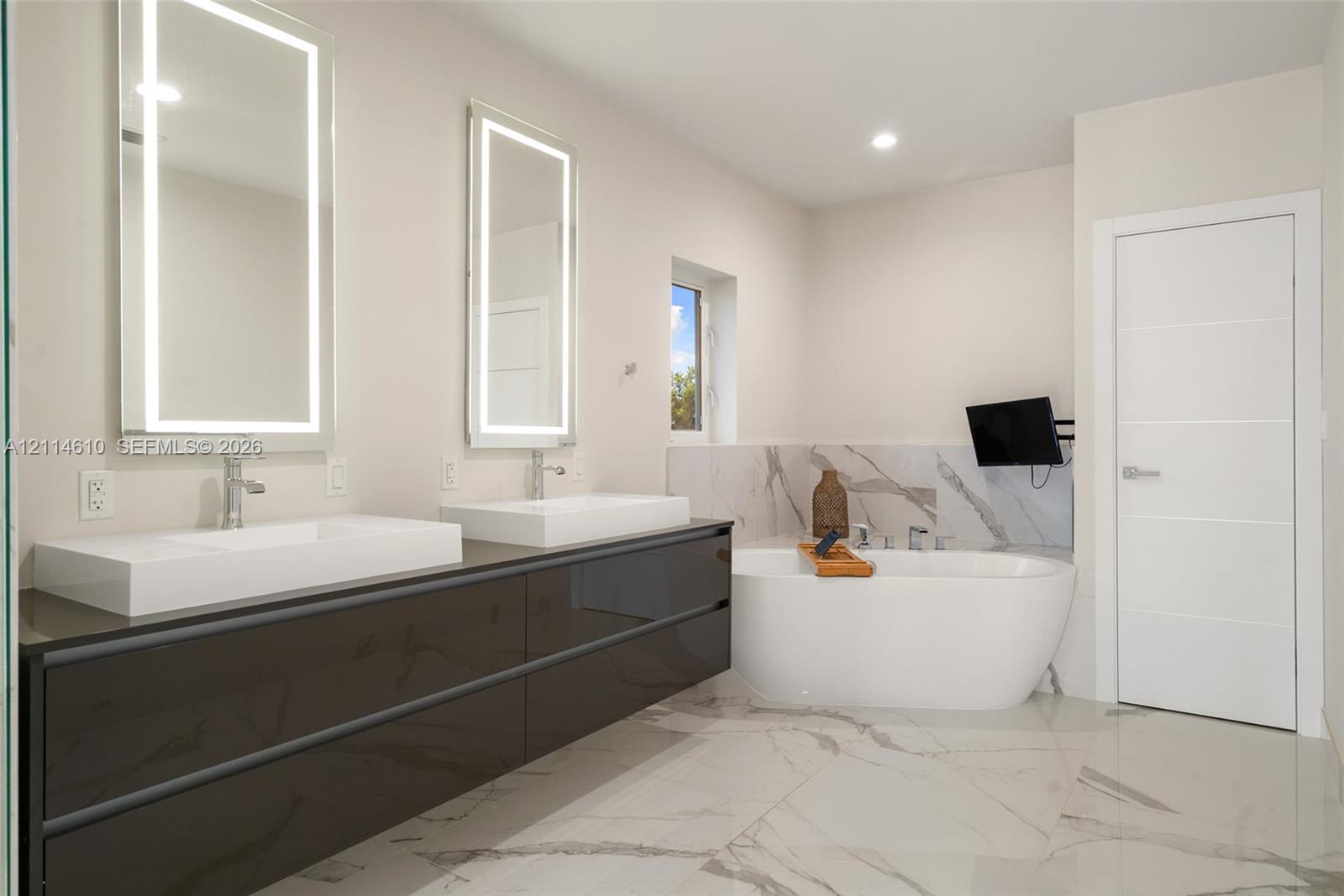 Floating dual vanity with integrated rectangular sinks, backlit wall-mounted mirrors, freestanding soaking tub, and large-format tile flooring with veining detail
