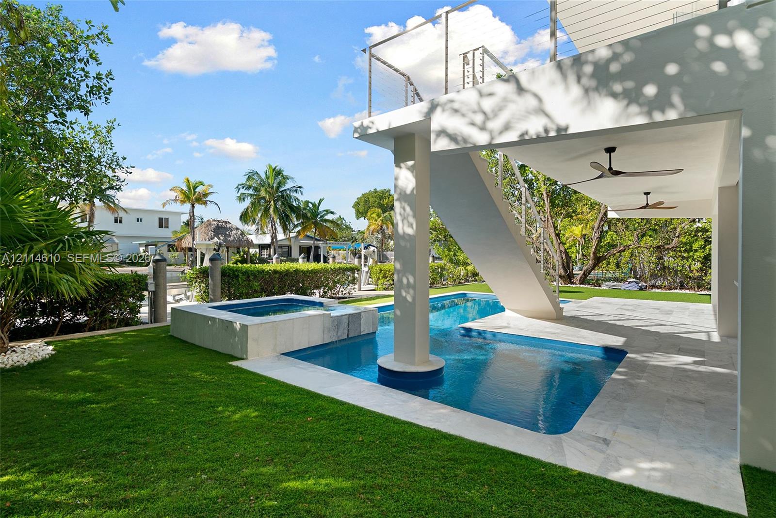 Swimming pool with integrated spa, covered patio with ceiling fans, and manicured lawn