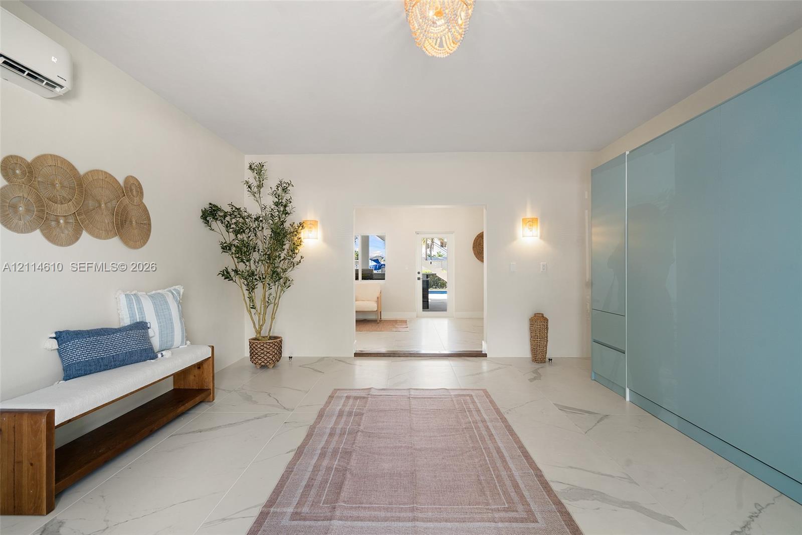 Large-format tile flooring with marble-style veining, floor-to-ceiling high-gloss panel cabinetry, wall-mounted ductless climate control system, tiered beaded chandelier, and dual wall-mounted light fixtures