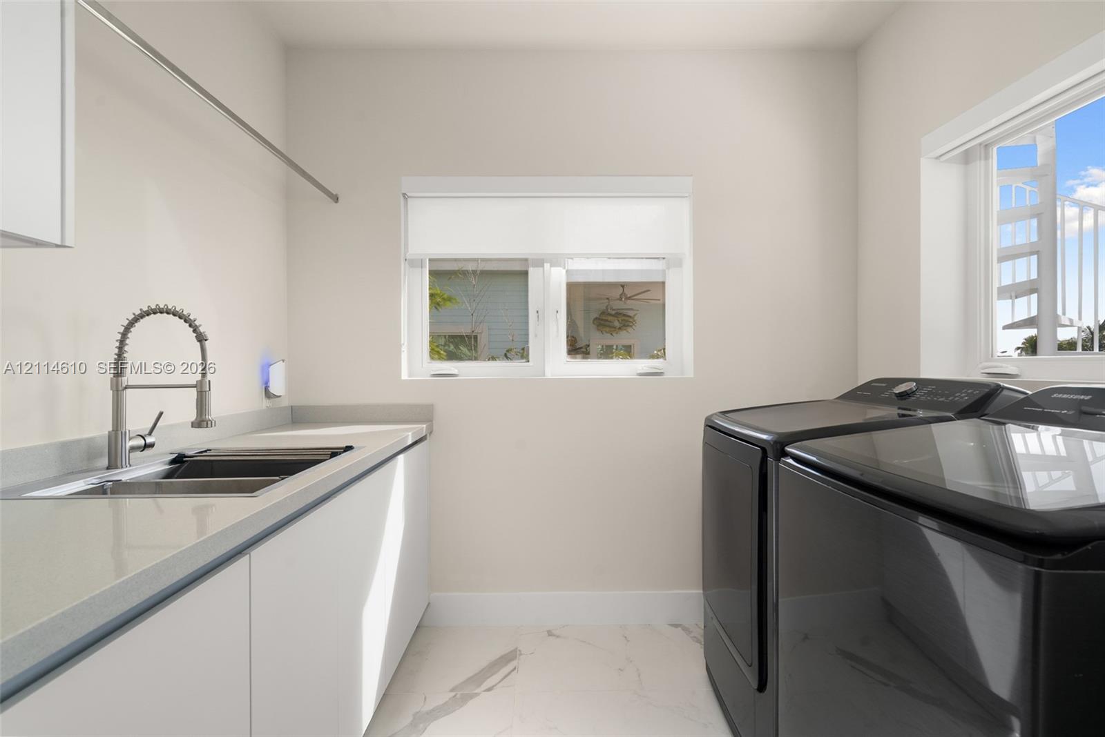 Utility space featuring stone-composite countertops, stainless steel sink with high-arc gooseneck faucet, flat-panel cabinetry, and large-format tile flooring
