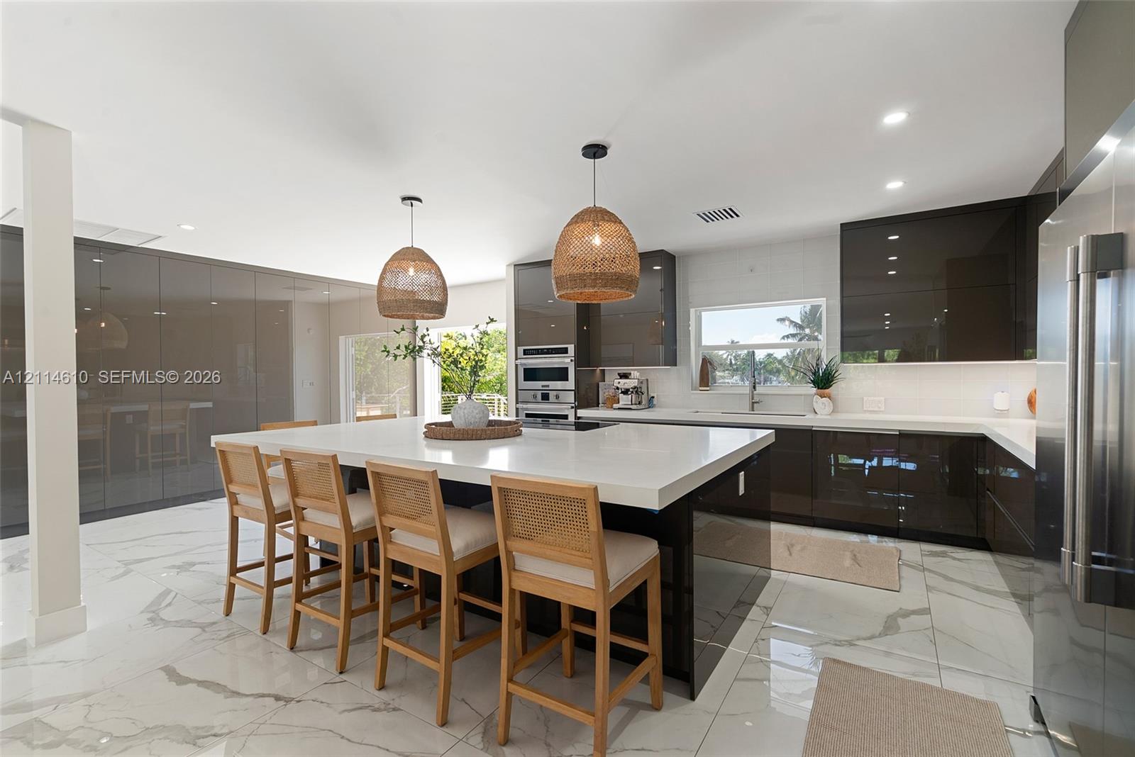 Modern kitchen featuring high-gloss cabinetry, a central island with a solid surface countertop, stone-finish flooring, built-in double wall ovens, and pendant lighting