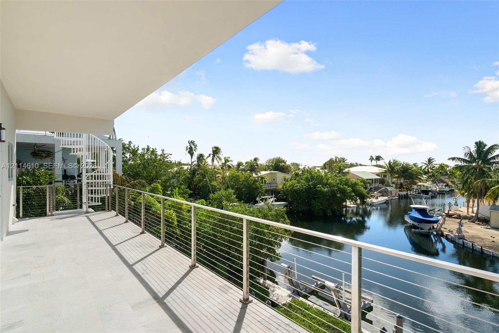 Covered balcony featuring stone-finish flooring, a white metal spiral staircase, and a stainless steel cable railing system overlooking a canal