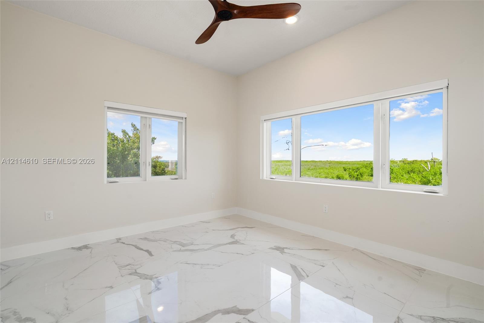 High-ceiling room featuring large windows with landscape scenery, polished stone-finish flooring, and a ceiling fan with wood-finish blades