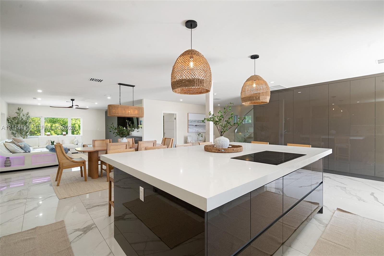 Large center island featuring a waterfall-edge quartz countertop, built-in induction cooktop, and glossy cabinetry