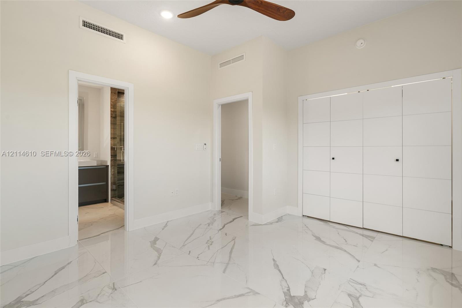 High-gloss porcelain tile flooring with marble-pattern veining, floor-to-ceiling multi-panel white cabinetry, and a ceiling fan with wood-finish blades